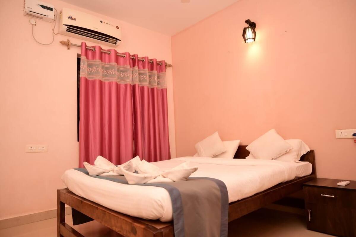 A single bed with white bedding, a wooden headboard, a bedside table, a nightstand, a wall-mounted air conditioner, and a wall-mounted light fixture.