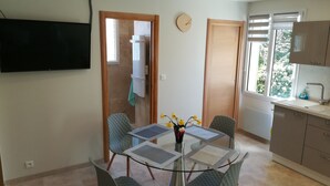 A compact kitchen with a sink, a flat-screen TV mounted on the wall, and a dining area with a glass table and four chairs. - In the Luberon, indulge yourself with a private spa and sauna (Reillanne)