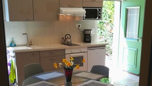 A modern kitchen with a dining area, including a round glass table with chairs, a vase with flowers, and a coffee maker. - In the Luberon, indulge yourself with a private spa and sauna (Reillanne)