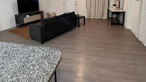 A modern living room with a flat-screen TV, a dark sofa, and a coffee table. There is a dining area with a small table and chairs. The room has a ceiling fan and a light fixture. - Charming 1-bedroom apartment in Leander, featuring AC, WiFi (Cedar Park)