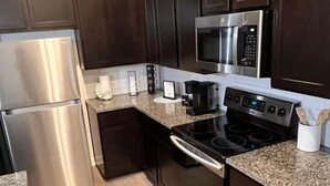 A modern kitchen with dark wood cabinets, stainless steel appliances, and a granite countertop. - Charming 1-bedroom apartment in Leander, featuring AC, WiFi (Cedar Park)
