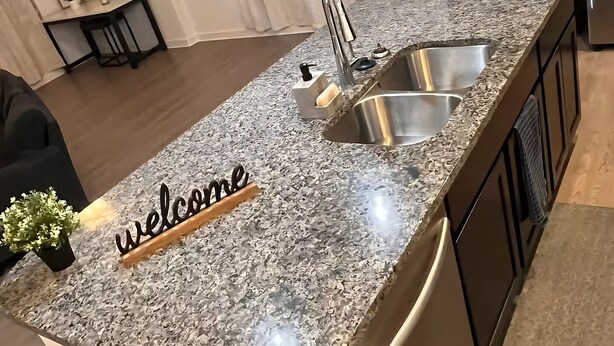A modern kitchen with a granite countertop, stainless steel sink, and a 'welcome' sign. - Charming 1-bedroom apartment in Leander, featuring AC, WiFi (Cedar Park)
