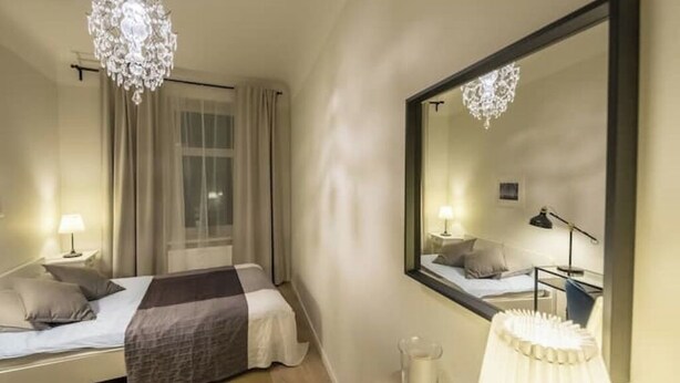 Une chambre d’hôtel avec un lit, une table de chevet, une lampe, un miroir et un lustre.