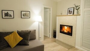 Un salon avec une cheminée, un canapé avec des coussins et deux tableaux encadrés au mur.