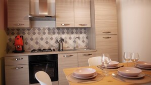 A modern kitchen with wooden cabinets, a gas stove, and a dining area with a table set for two. - "Cozy Apartment Near the Sea - Ideal for Holidays" (Balestrate)