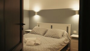 A neatly made bed with a quilted cover, two pillows, and a folded towel on the side. There are two bedside tables with lamps on either side of the bed. The room has a simple, clean design with a neutral color scheme. - "Cozy Apartment Near the Sea - Ideal for Holidays" (Balestrate)