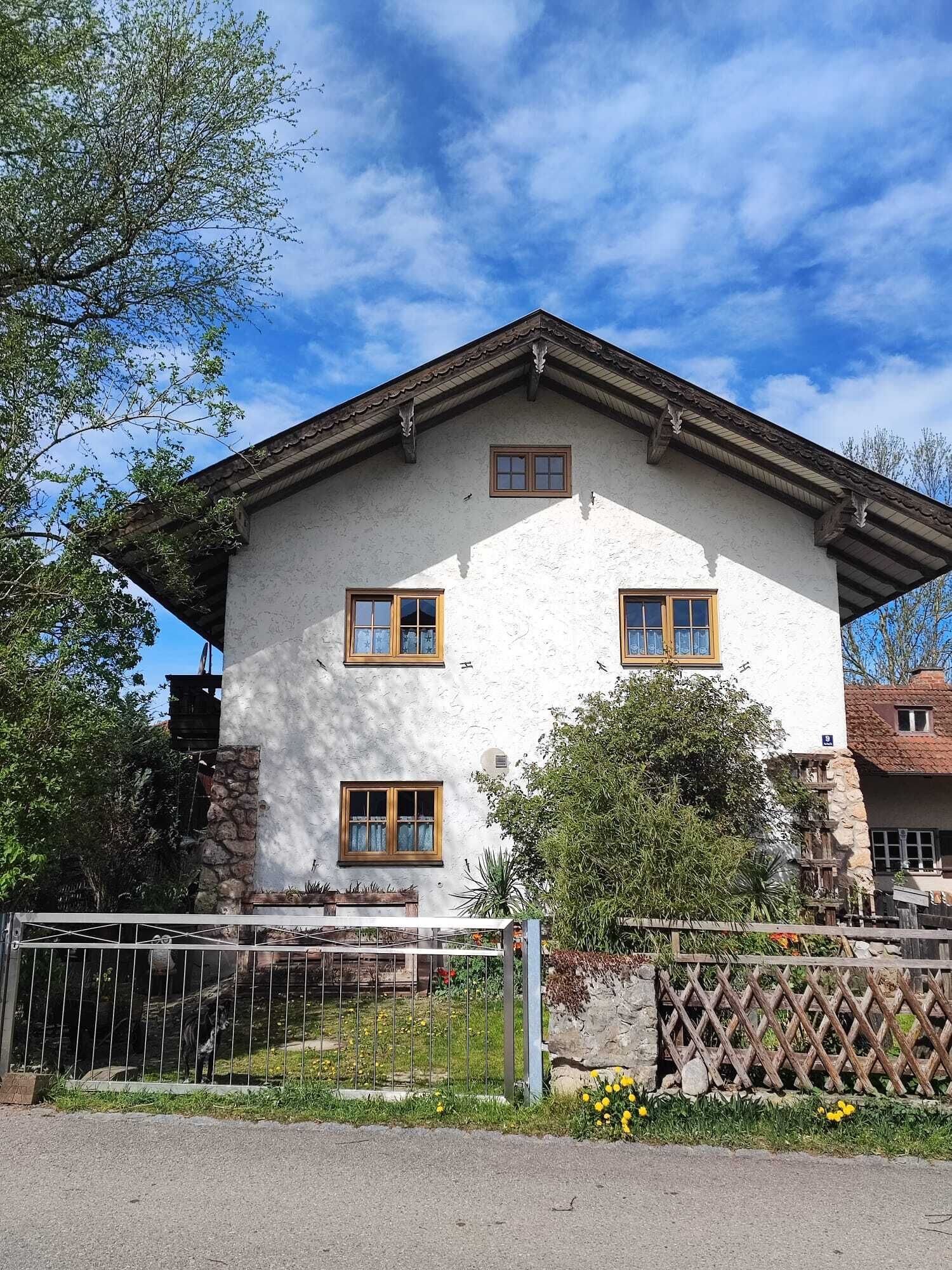 Ein zweistöckiges Gebäude mit weißer Fassade und braunen Verzierungen, mit drei Fenstern und einem kleinen Balkon.
