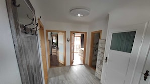 Un couloir avec un plancher en bois, une porte blanche dotée d’une fenêtre et un miroir sur le côté gauche.