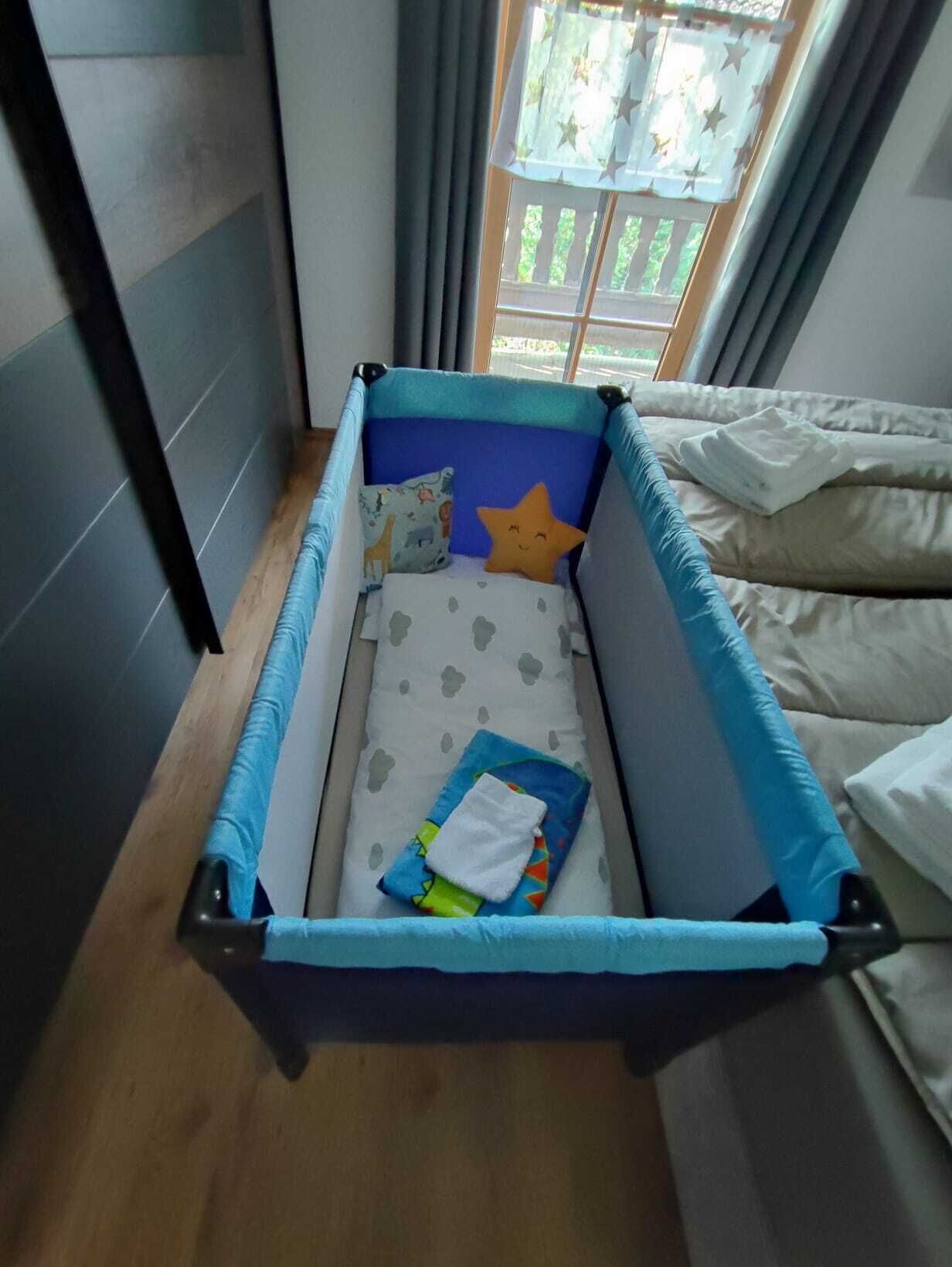 Un petit espace de jeu clos, avec un matelas bleu et blanc, un coussin en forme d’étoile et une couverture.
