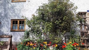 Une maison rustique avec trois fenêtres, un jardin aux fleurs multicolores et une sculpture en bois.