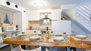 Une cuisine moderne avec des meubles blancs, une table à manger en bois pour quatre personnes et une cuisinière intégrée.