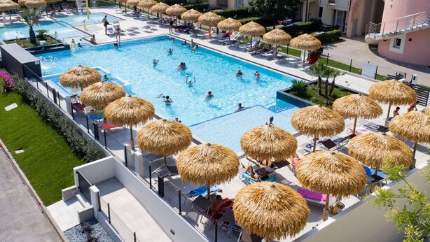 A swimming pool with multiple lanes, surrounded by lounge chairs and thatched umbrellas.