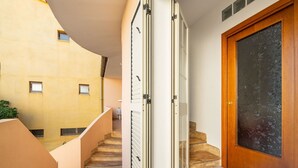 Un interior moderno con una escalera que conduce a un segundo piso, una puerta de madera y una puerta de cristal con diseño texturizado.