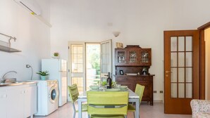 Una cocina compacta con lavadora, zona de comedor con mesa y sillas, y un mueble de madera con puertas de cristal.