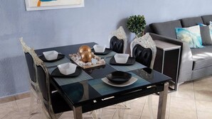 Une table à manger entourée de chaises en verre transparent, un tableau abstrait bleu accroché au mur et, au fond, un canapé gris agrémenté de coussins.