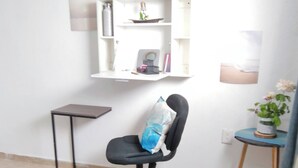 Une petite pièce, bien rangée, avec un lit, un bureau, une chaise et une étagère où sont posés des objets personnels.