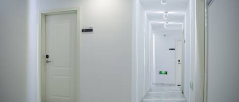Un couloir propre et moderne, aux murs blancs et au sol en marbre, qui mène à plusieurs portes et à un panneau indiquant la sortie de secours.