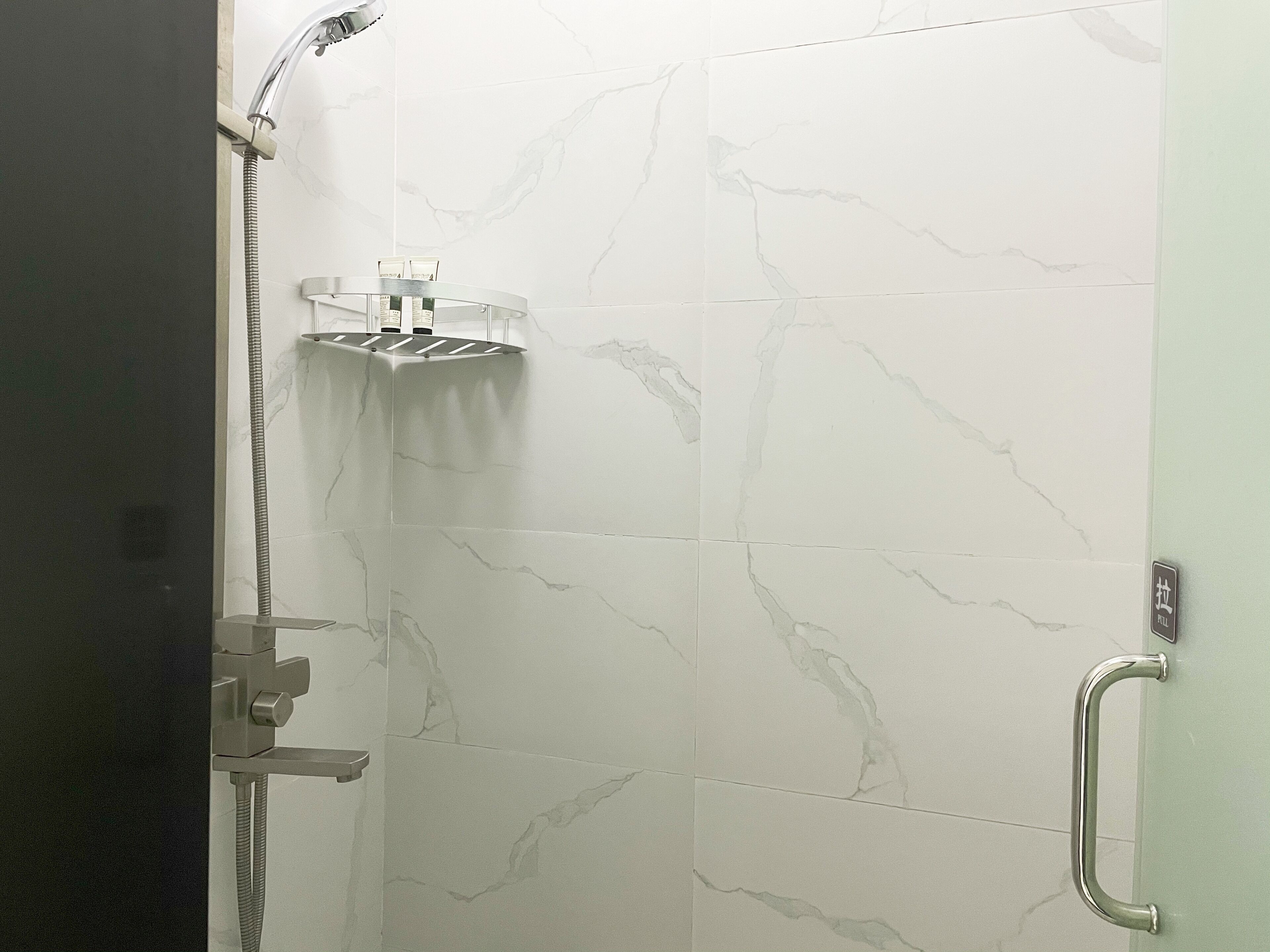 Zona de ducha con cabezal de ducha de mano, panel de control en la pared y un perchero.