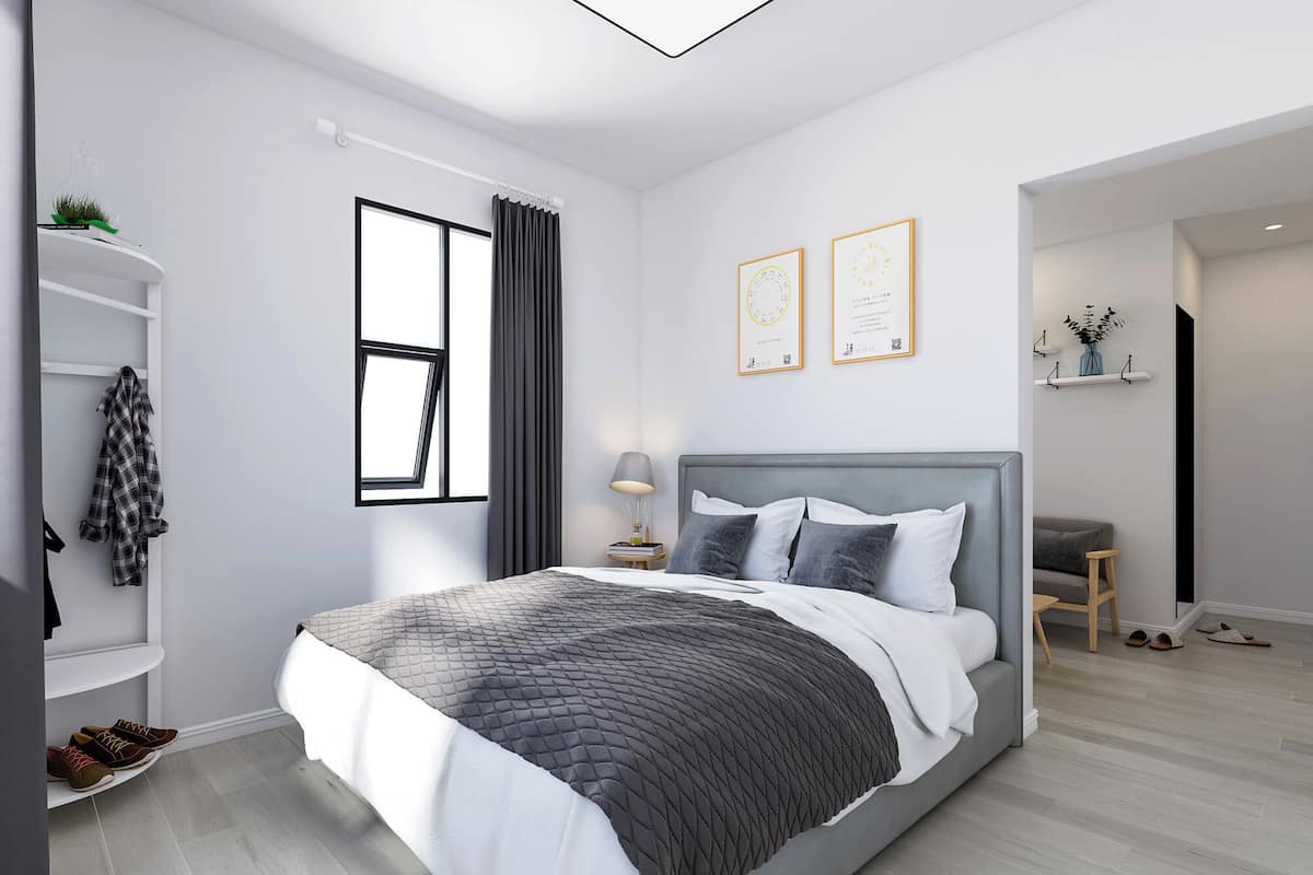 Ein modernes Schlafzimmer mit Bett, Nachttisch, Fenster mit Vorhängen und einer kleinen Sitzecke mit Sessel und Tisch.