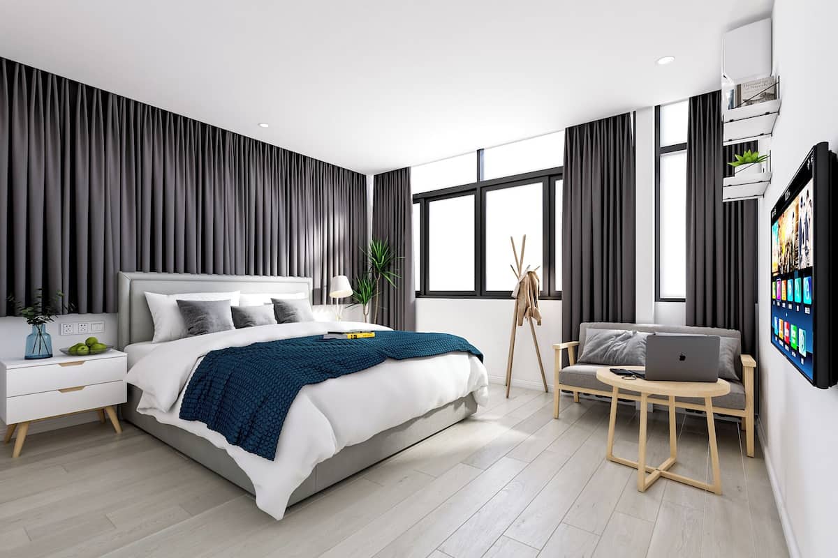 Ein modernes Schlafzimmer mit einem großen Bett, Nachttischen, einem Schreibtisch mit einem Laptop und einem großen Fenster.