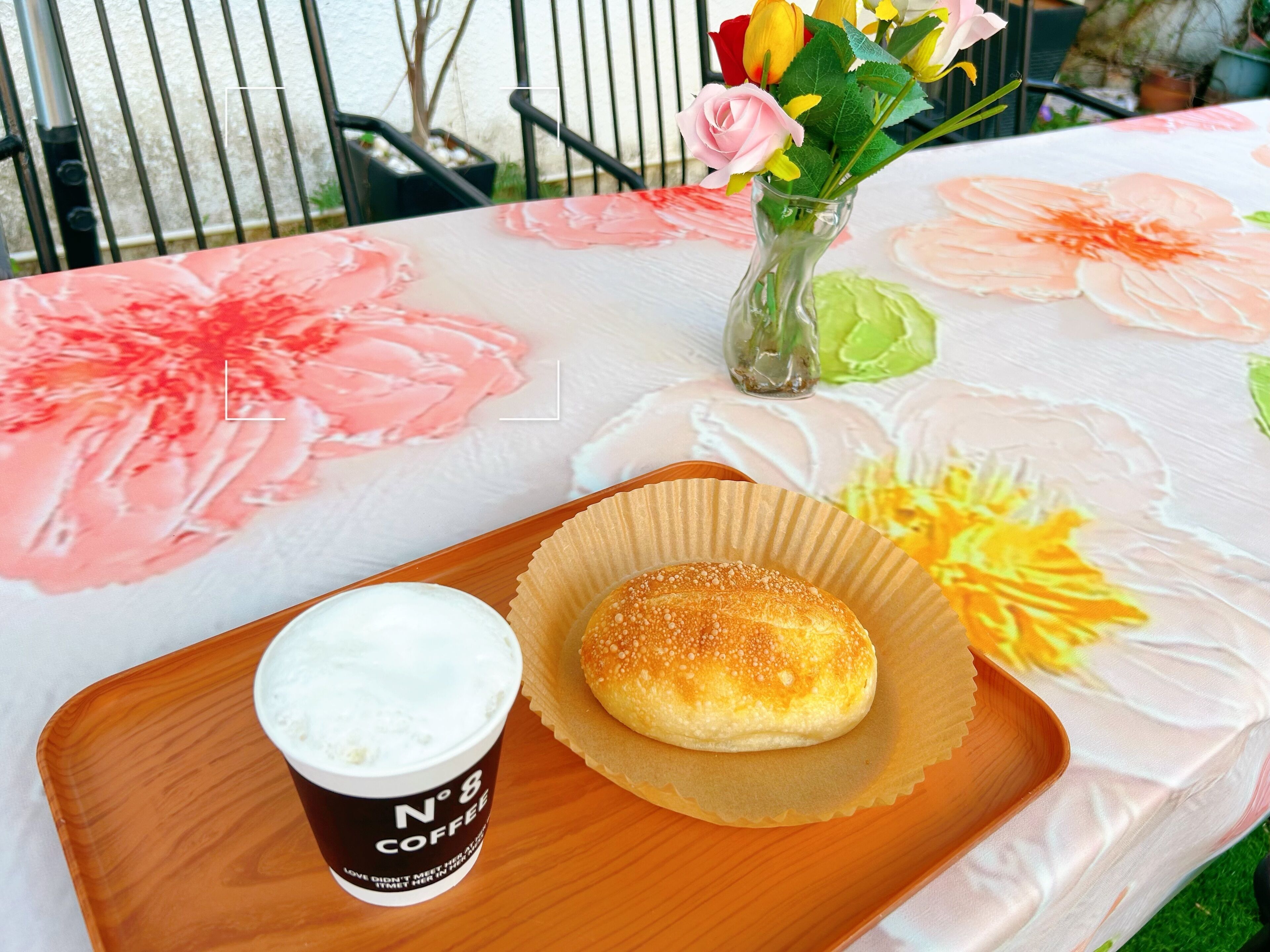 Ein Tisch mit einer blumigen Tischdecke, einer Kaffeetasse und einem Gebäck auf einem Holftablett.
