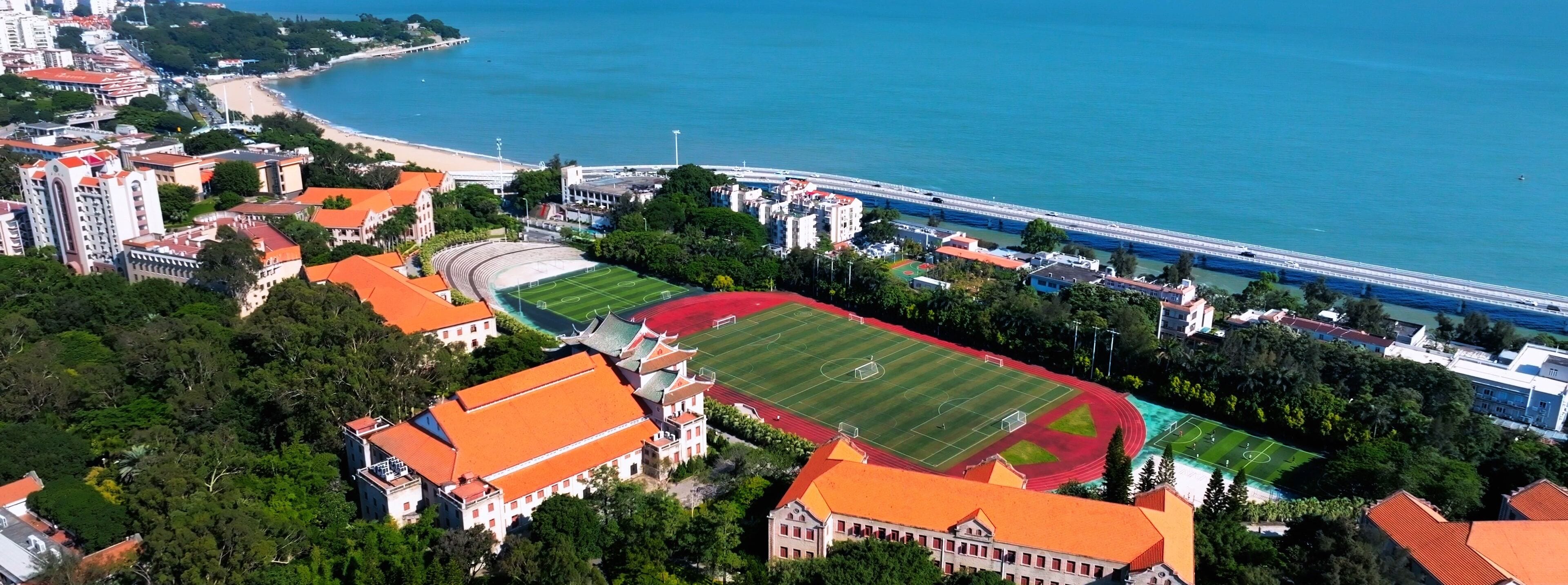 An aerial view of a coastal area with a large sports field surrounded by buildings and a beach.