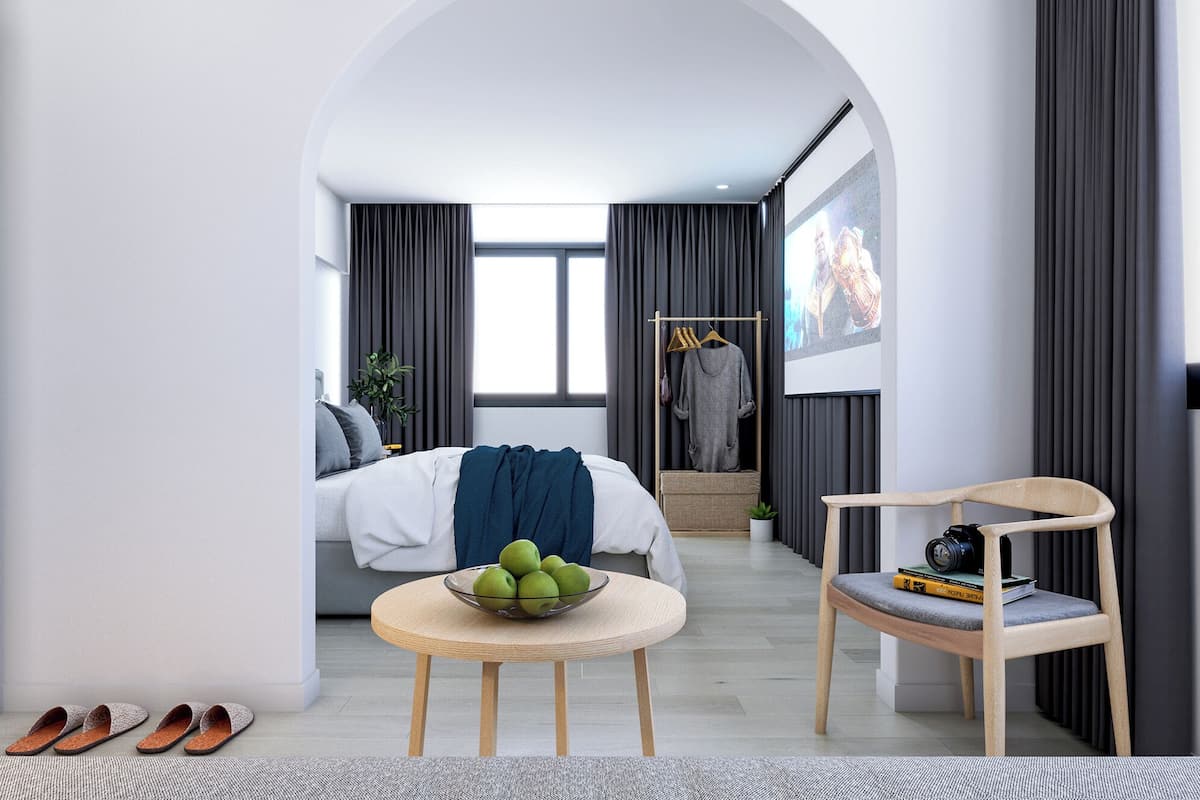 Ein modernes Hotelzimmer mit Bett, einer Sitzecke mit Tisch und Stuhl, einem Kleiderständer und einem Fernsehbildschirm.