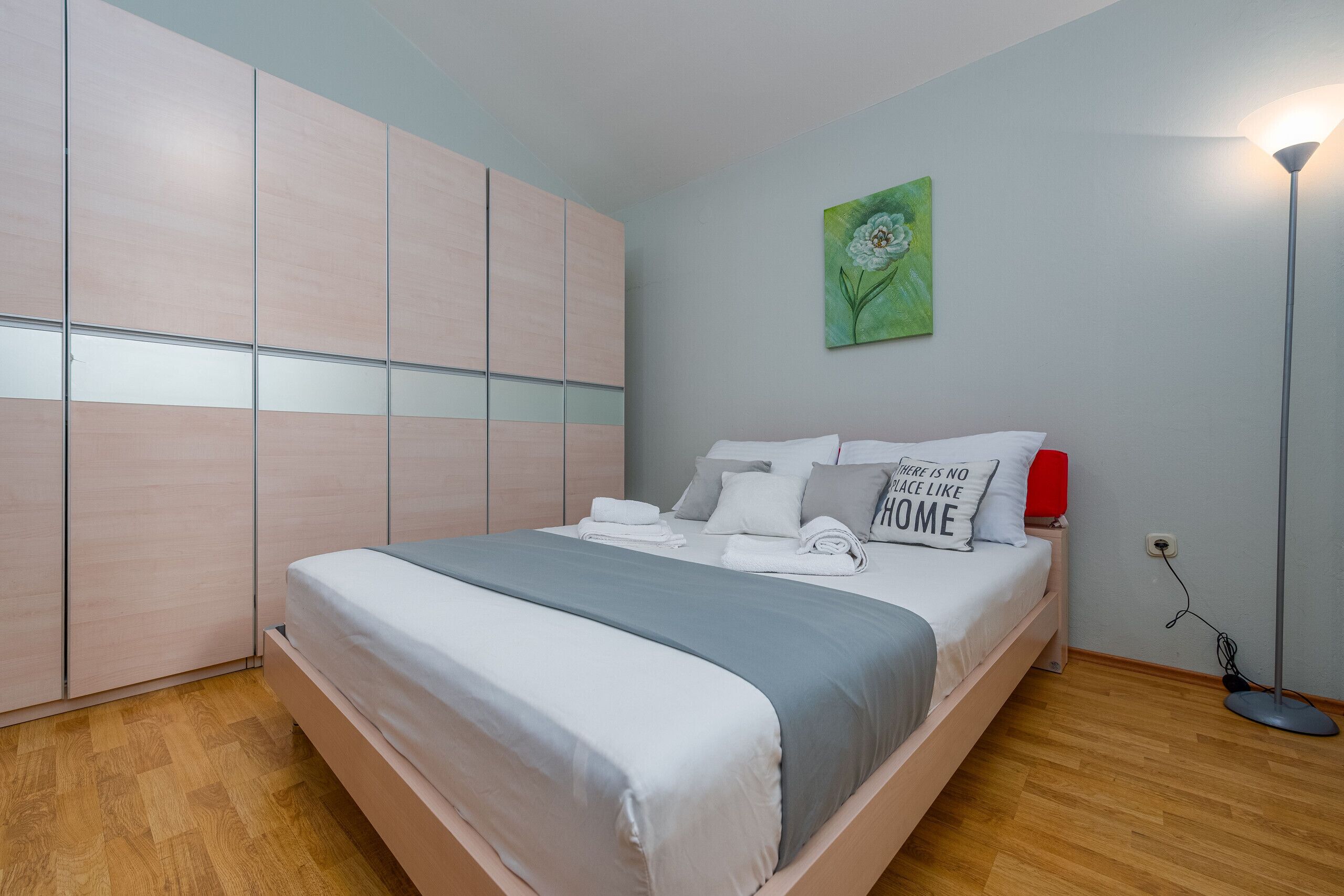 Un dormitorio con cama, armario, un cuadro y una lámpara de pie.
