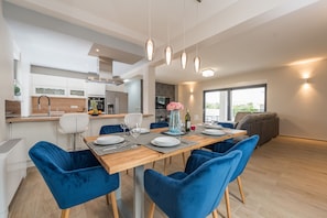 A modern kitchen with white cabinets, a dining area with blue velvet chairs, and a large window providing natural light. - Villa Nika Zadarvillas (Zadar)