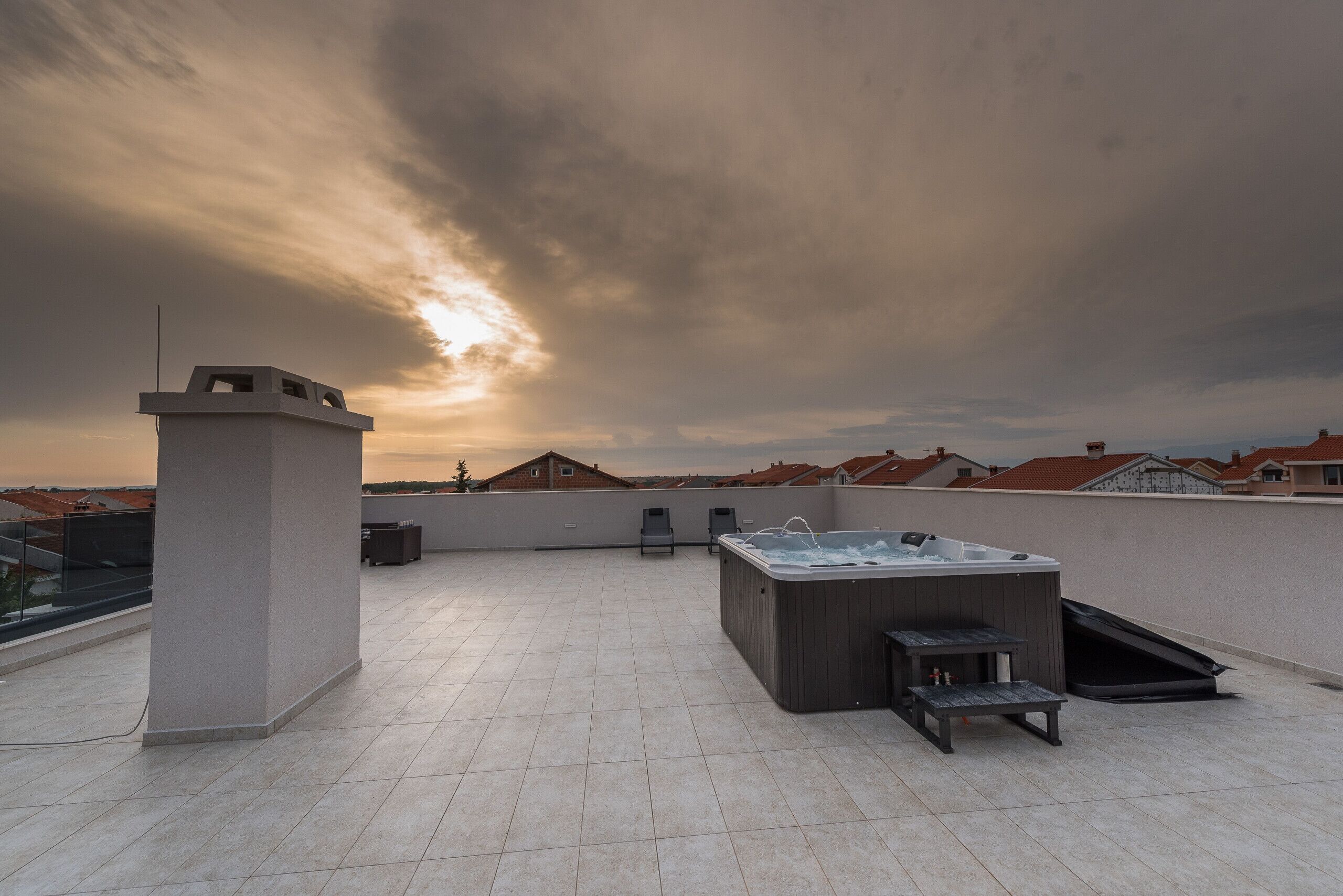 A rooftop terrace with a hot tub, seating area, and a view of the cityscape during sunset.