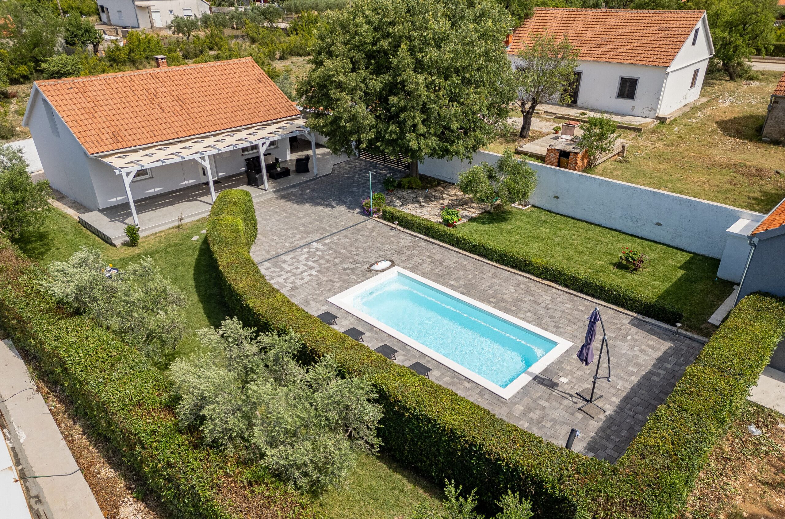 Een woonhuis met een zwembad, overdekt terras en een goed onderhouden tuin.