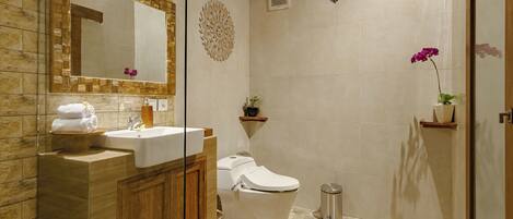 Un baño con tocador de madera, lavamanos, inodoro y zona de ducha.