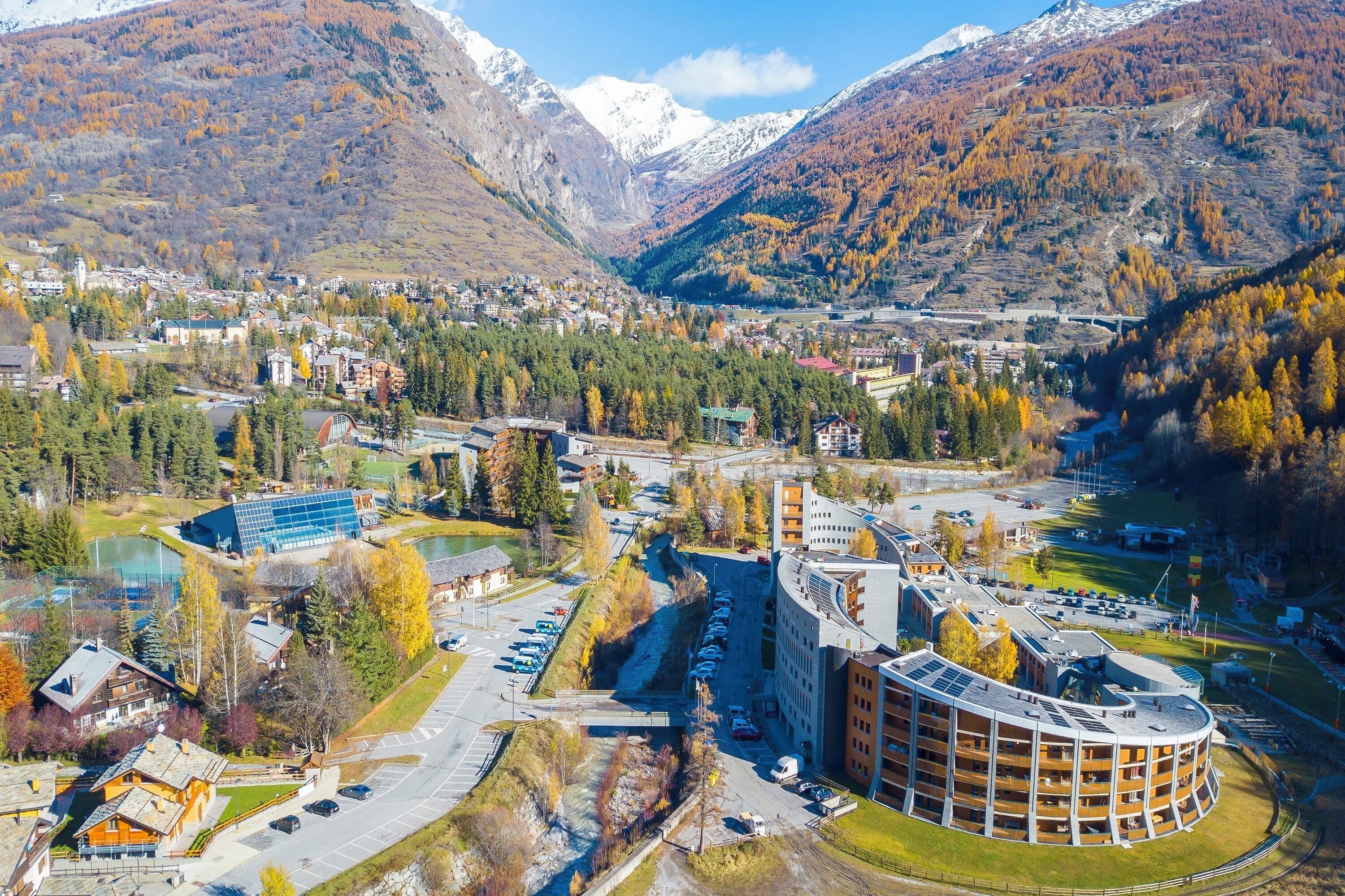 A modern hotel with a circular building, a parking lot, and a river in the background.