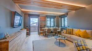 Un soggiorno moderno con soffitto in legno, zona pranzo e divano con cuscini gialli.