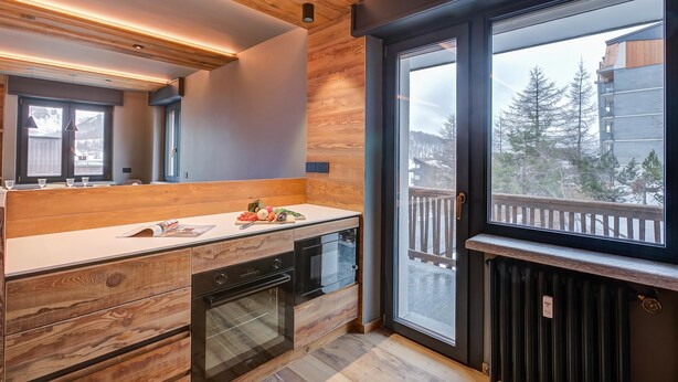 Una cucina moderna con mobili in legno, forno integrato e un'ampia finestra che si affaccia su un balcone e alberi.