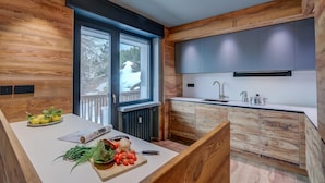 Una cucina moderna con mobili in legno, un piano di lavoro bianco e un'ampia finestra che si affaccia su un paesaggio innevato.