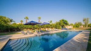 A swimming pool with lounge chairs and umbrellas, surrounded by greenery and palm trees. - Villa Vallone Luxury With Pool (Galatina)
