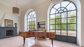 A spacious room with a polished floor, a grand piano, a fireplace, and large arched windows offering a view of greenery. - Villa Vallone Luxury With Pool (Galatina)