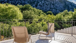 Un balcon avec des fauteuils en osier, un mur en pierre et une vue sur un paysage montagneux.