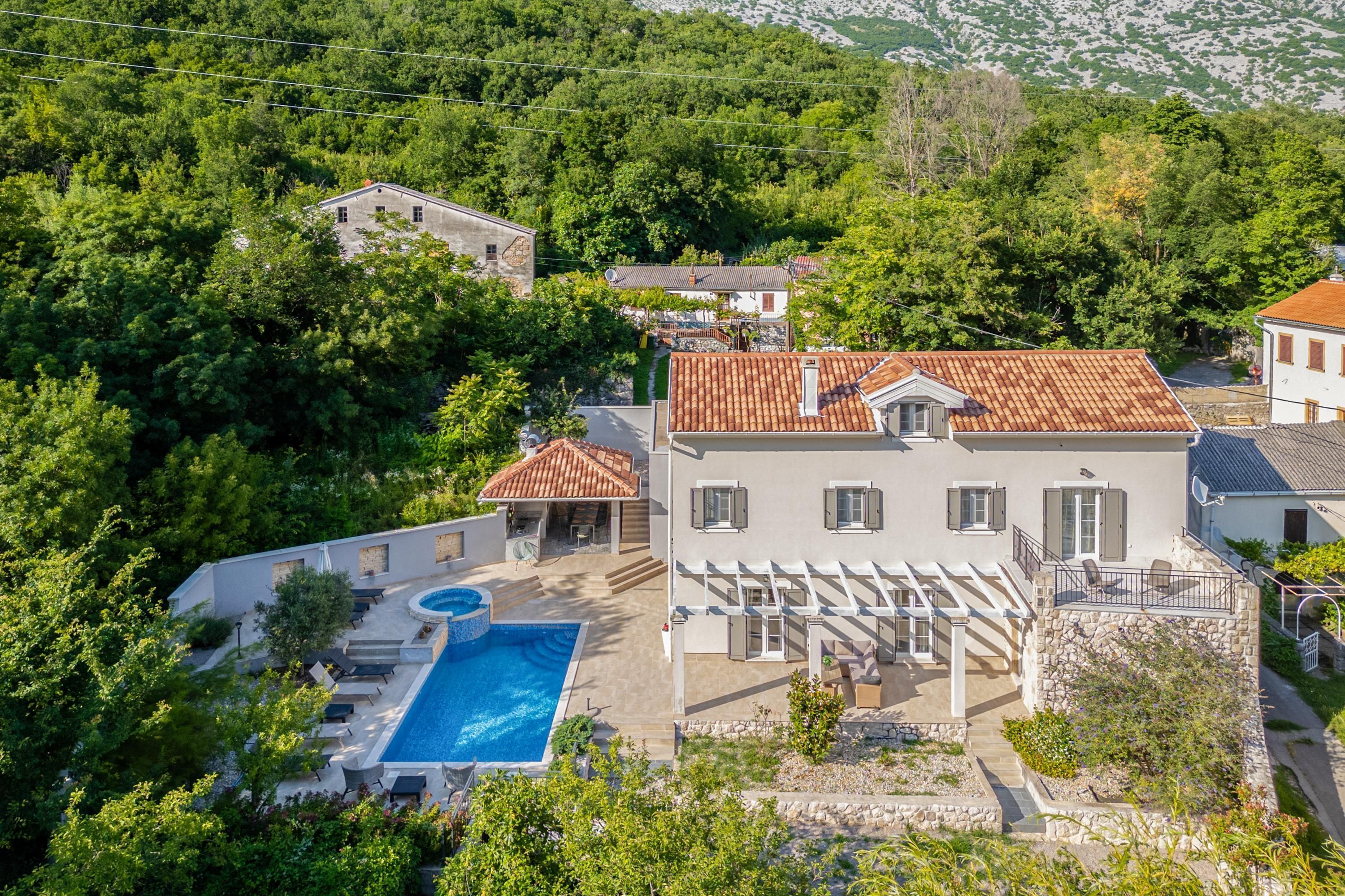 A villa with a swimming pool, surrounded by lush greenery and a mountainous backdrop.