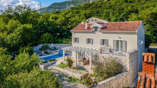 Une maison à deux étages avec une piscine, un espace salon extérieur et un mur en pierre.