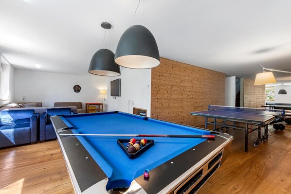 A pool table with balls, a ping pong table, and a billiards table in a room with wooden flooring and a brick wall. - Maison Montagne in Samedan (Samedan)