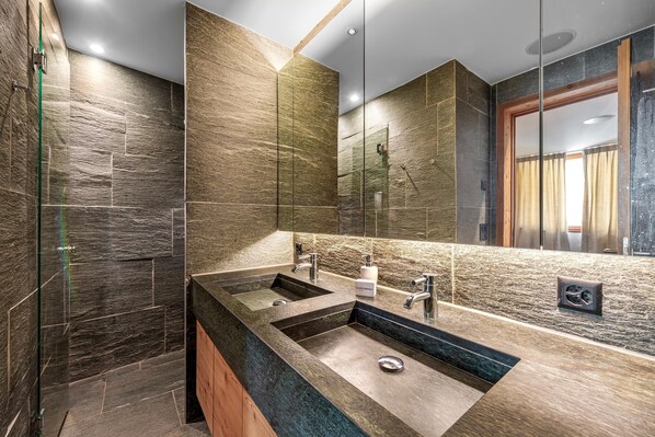 Une salle de bain moderne avec un grand lavabo, deux robinets et une douche à parois de verre.