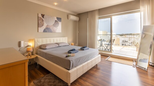 Ein modernes Schlafzimmer mit einem großen Bett, Nachttischen, einem kleinen Tisch mit einer Lampe, einer Wand-Klimaanlage und einem großen Fenster mit Blick ins Freie.