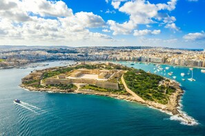 An aerial view of a coastal city with a prominent fort, a marina with boats, and a densely built urban area in the background. - Modern Penthouse Savoy Garden in Gzira (Gzira)