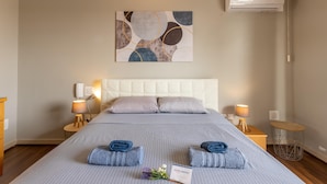 Ein Hotelzimmer mit einem großen Bett, zwei Nachttischlampen, einer Wand-Klimaanlage und einem Gemälde über dem Bett.