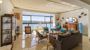A spacious living room with a large window, a sofa, chairs, a cabinet, and a decorative mirror. - Magnificent Sunny Seafront Apart Sliema (Sliema)