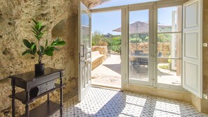 Una habitación con pared de piedra, una planta en maceta, una mesa de madera y vistas a un patio exterior.