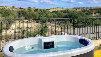 Relax in the hot tub on the outdoor balcony with a serene view of the hilly landscape.