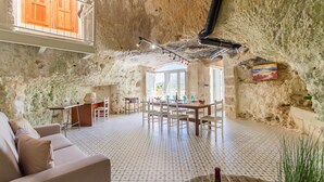 Amplia sala de estar con techo alto, paredes de piedra, una mesa de comedor con sillas, un sofá y suelo de baldosas.